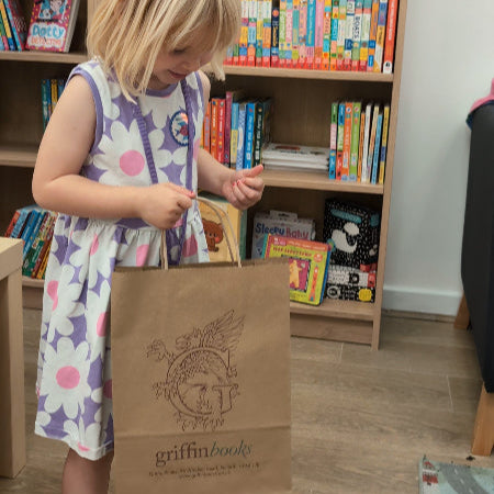 Child holding a brown paper bag with 'griffin books' logo in front of a bookshelf filled with books.