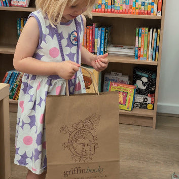 Young girl opening a brown paper bag with 'griffin books' logo in a library setting.